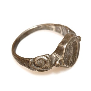 May include: A silver signet ring with an ornate design and a hexagonal bezel. The ring is worn and has a patina.
