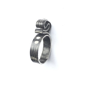 Puede incluir: Un anillo de plata con un diseño único y abstracto. El anillo está hecho de una banda delgada y retorcida de metal con un remolino en la parte superior. La banda está decorada con pequeños puntos blancos.