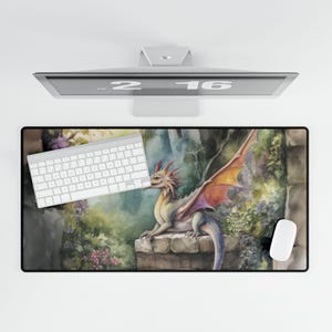 May include: A rectangular mouse pad featuring a watercolor illustration of a dragon with orange and purple wings, resting on a stone wall. The dragon is set against a backdrop of lush greenery and a stone structure. A white keyboard and mouse are on the pad.