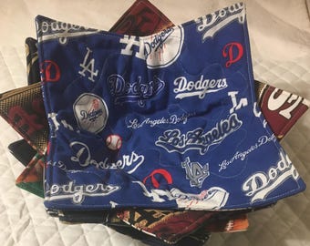 May include: A stack of quilted fabric bowl cozies. The top cozy is blue with white text and logos for the Los Angeles Dodgers baseball team. Other cozies in the stack have different patterns and colors.