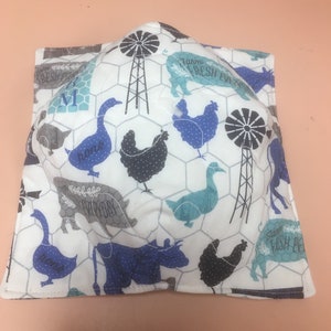 May include: A square, white bowl cozy with a farm animal print. The print includes blue, gray, and black chickens, cows, and geese, along with windmills and the words "Farm Fresh Everyday". The cozy is designed to hold a bowl.
