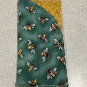May include: A fabric item with a green background and a pattern of yellow and black bees. The item has a curved edge and a yellow patterned interior.