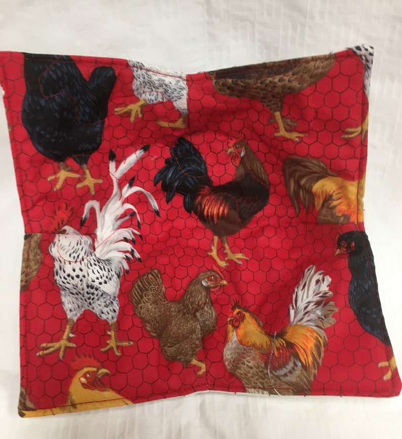 May include: A square, quilted fabric bowl cozy featuring a vibrant red background with a chicken wire pattern. The fabric is adorned with various illustrations of chickens and roosters in shades of brown, black, white, and yellow.