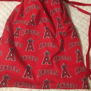 Puede incluir: Bolsa roja con cord&oacute;n con un patr&oacute;n repetido de la palabra "ANGELS" y el logotipo del equipo en blanco y negro. La bolsa tiene cordones rojos y est&aacute; hecha de tela.