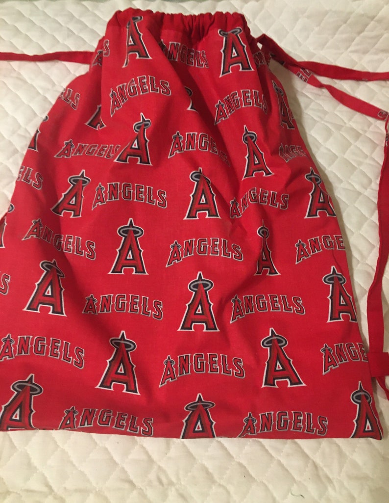 Puede incluir: Bolsa roja con cord&oacute;n con un patr&oacute;n repetido de la palabra "ANGELS" y el logotipo del equipo en blanco y negro. La bolsa tiene cordones rojos y est&aacute; hecha de tela.
