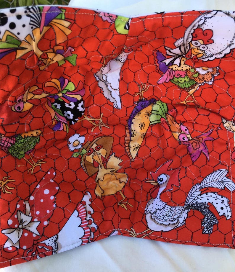 May include: A quilted fabric with a vibrant red chicken wire pattern. The fabric is adorned with whimsical, colorful chicken illustrations. The chickens are depicted in various poses and outfits, adding a playful touch to the design. The fabric is likely used for crafting or home decor.