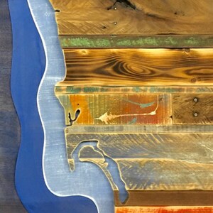 May include: A wooden wall art piece featuring a blue outline of a coastline. The wood is reclaimed and has a variety of colors and textures.