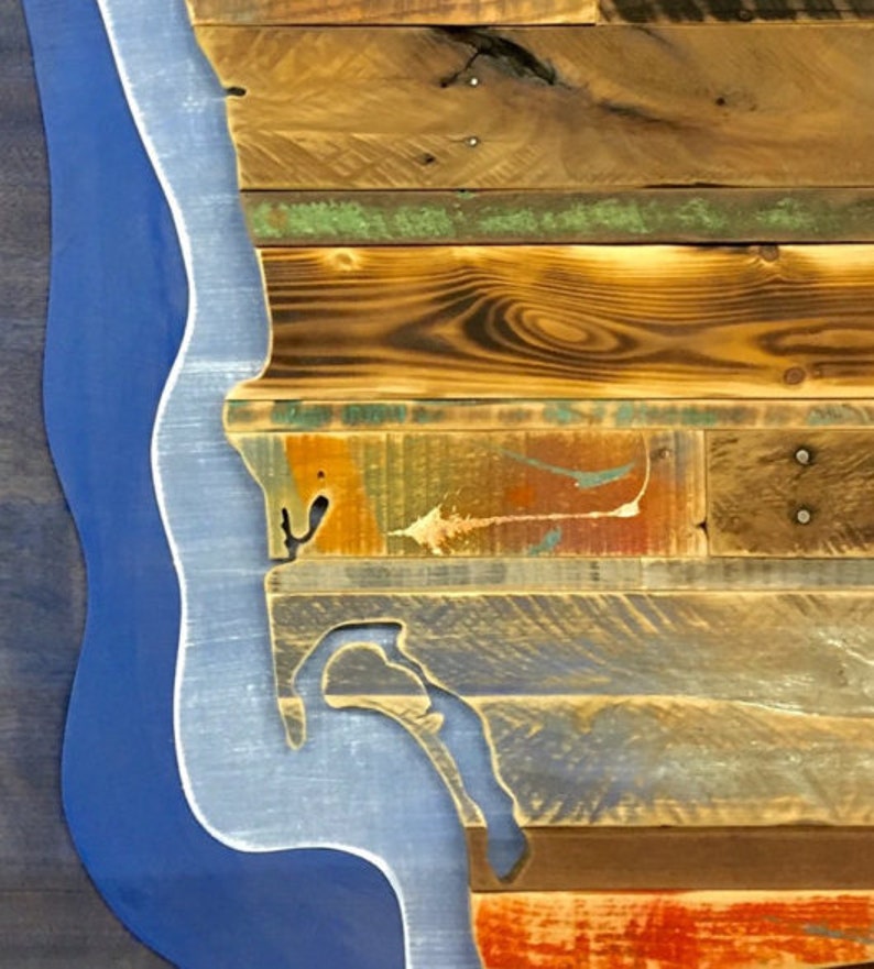 May include: A wooden wall art piece featuring a blue outline of a coastline. The wood is reclaimed and has a variety of colors and textures.
