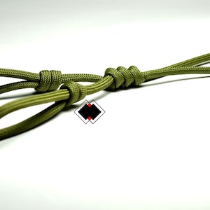 May include: A green paracord loop with a knot in the centre. The loop is tied in a way that creates two smaller loops on either side of the knot.