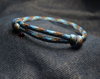 May include: A blue and brown camouflage paracord bracelet with a knot on one end.