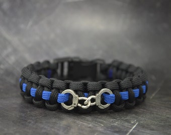 May include: Black and blue paracord bracelet with silver handcuff charms.