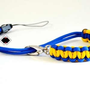 May include: A blue and yellow paracord lanyard with a metal clasp. The lanyard is made of two strands of paracord, one blue and one yellow, that are braided together.