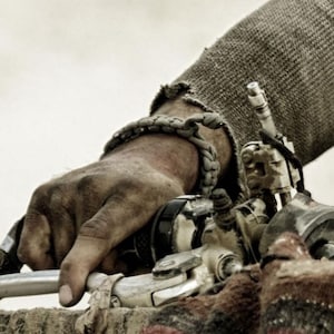 May include: A close-up of a hand wearing a braided leather bracelet, gripping a motorcycle handlebar. The hand is dirty and the leather bracelet is worn.