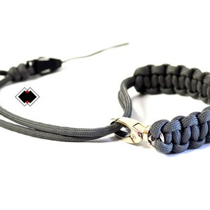May include: A grey paracord bracelet with a silver clasp. The bracelet is made of woven paracord and has a simple design.