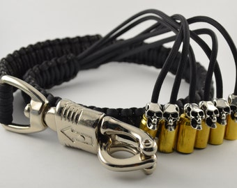 May include: Black paracord bracelet with a silver clasp and six gold-colored bullet casings, each topped with a silver skull. The bracelet is a unique accessory.