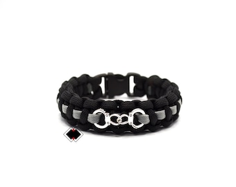 May include: Black and gray paracord bracelet with a silver handcuff charm.