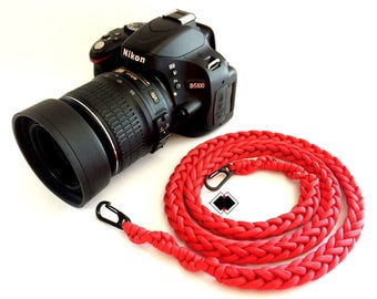 May include: A black Nikon D5100 camera with a lens attached and a red braided camera strap with a metal clasp.