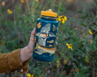 May include: A teal water bottle with a yellow cap, featuring illustrations of a bird, fish, and butterflies. The bottle is held against a backdrop of yellow wildflowers and greenery.