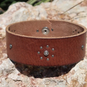 May include: A brown leather bracelet with silver studs and a single rhinestone in the center.