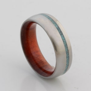 May include: A silver ring with a thin turquoise inlay and a red wood inlay.
