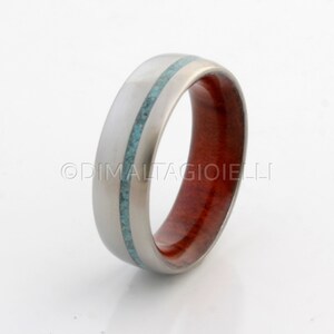 May include: A titanium ring with a turquoise inlay and a red wood band.