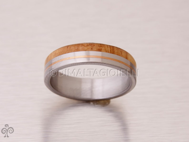 May include: A silver ring with a band of wood and two thin gold bands.