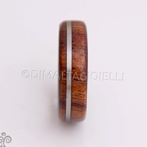 May include: A wooden ring with a silver inlay. The ring is brown with a reddish hue and has a smooth finish.