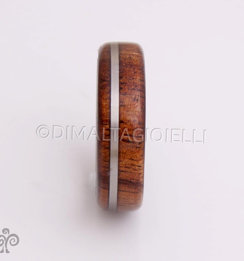 May include: A wooden ring with a silver inlay. The ring is brown with a reddish hue and has a smooth finish.