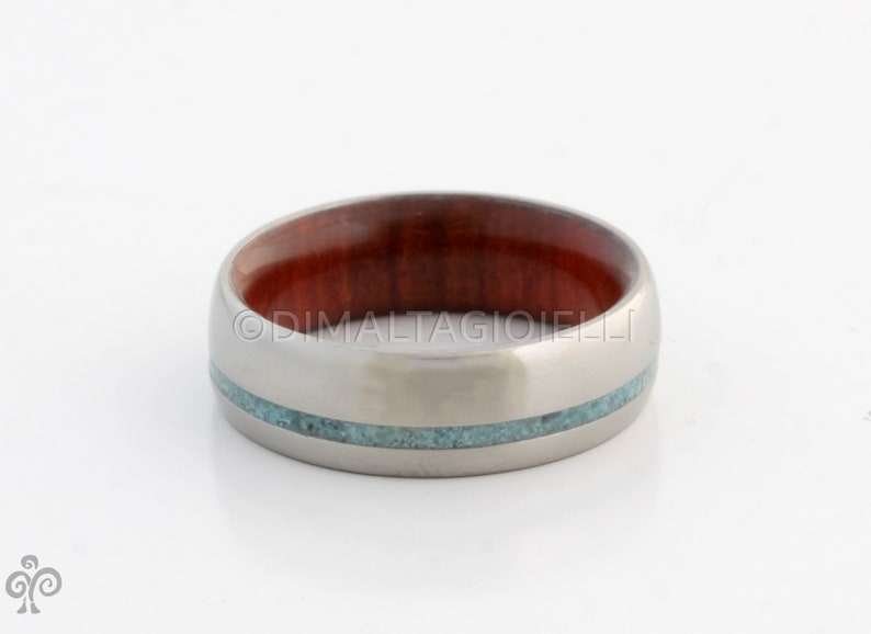 May include: A silver titanium ring with a red wood inlay and a turquoise inlay.