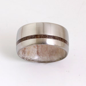 May include: A silver ring with a brown wood inlay. The ring is wide and has a rounded profile.