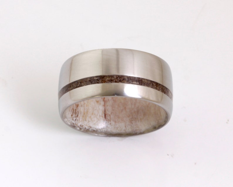 May include: A silver ring with a brown wood inlay. The ring is wide and has a rounded profile.