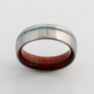 May include: A silver ring with a thin turquoise inlay and a red wood inlay.