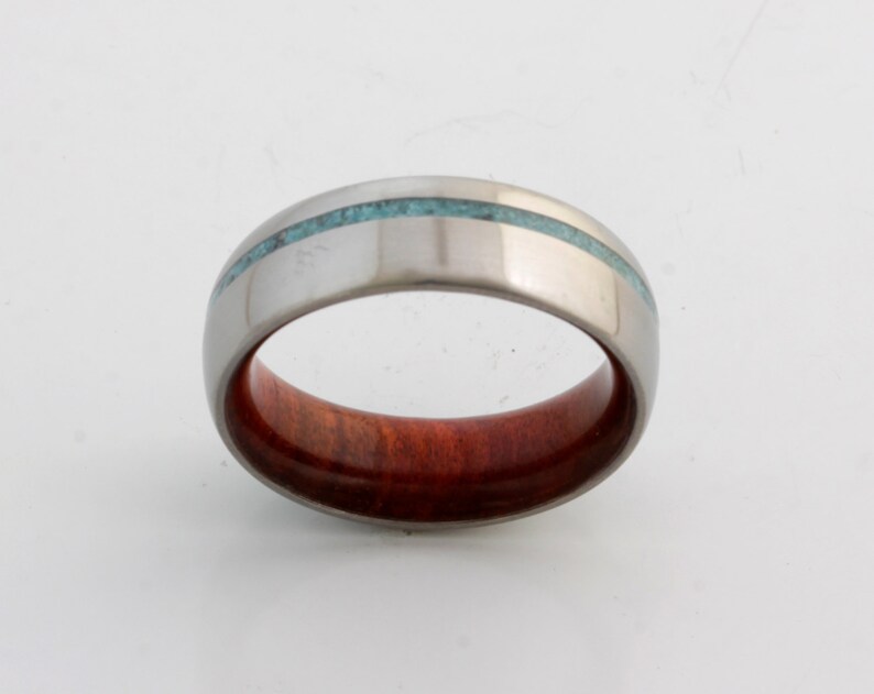 May include: A silver ring with a thin turquoise inlay and a red wood inlay.