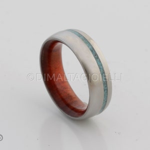 May include: A silver titanium ring with a red wood inlay and a turquoise inlay.