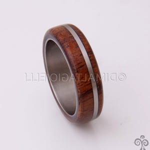 May include: A wooden ring with a silver inlay. The ring is brown and has a natural wood grain.