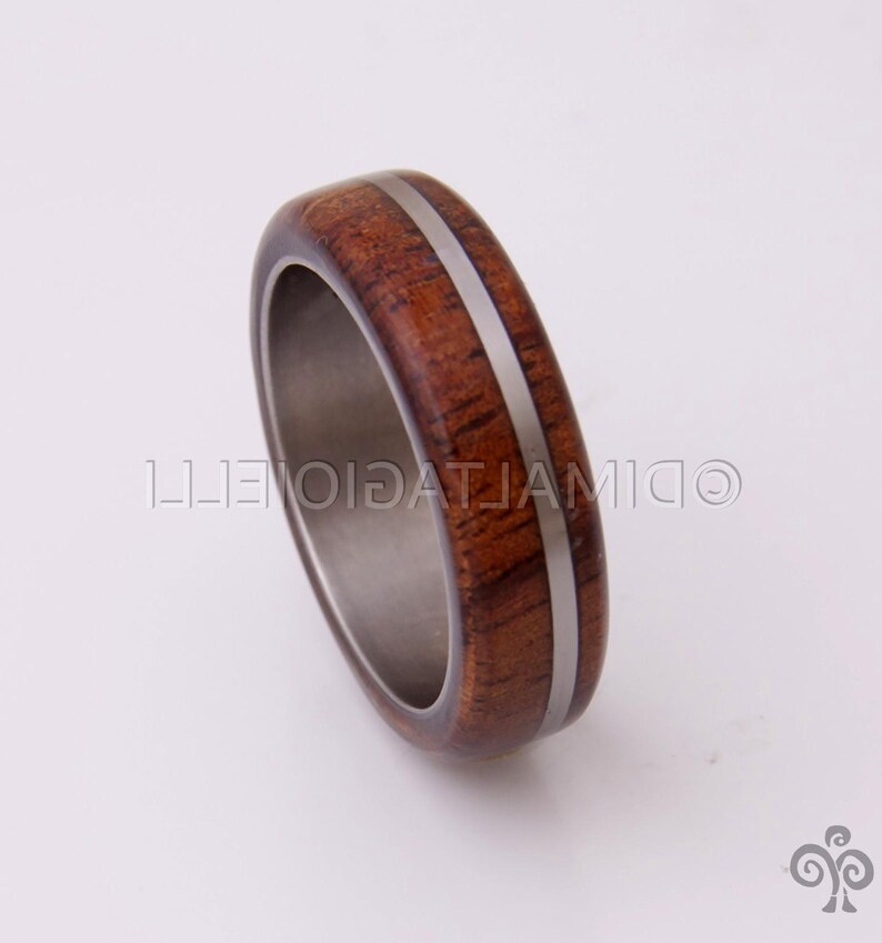 May include: A wooden ring with a silver inlay. The ring is brown and has a natural wood grain.