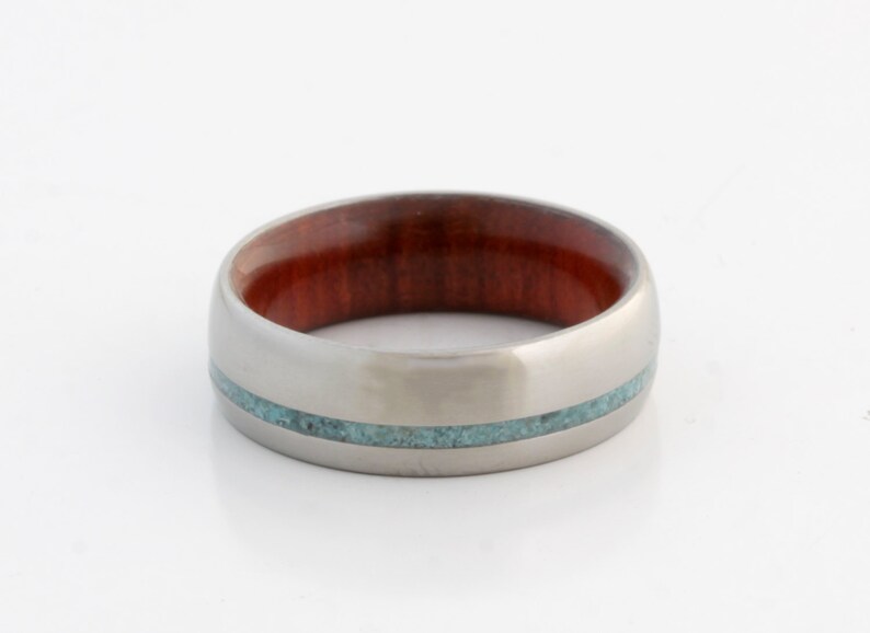 May include: A silver ring with a band of reddish-brown wood and a thin turquoise inlay.