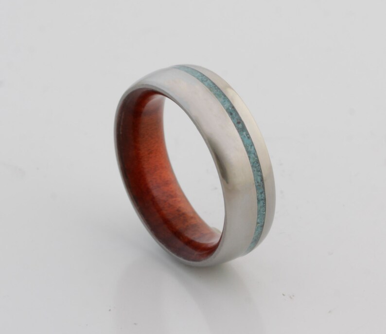May include: A silver ring with a thin turquoise inlay and a red wood inlay.
