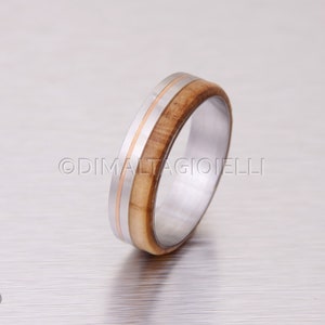 May include: A silver and wood ring with a thin band of rose gold. The ring is made of stainless steel and olive wood.