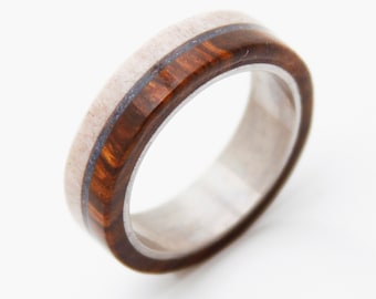 May include: A wooden ring with a brown and white wood inlay. The ring is made of stainless steel and has a polished finish.
