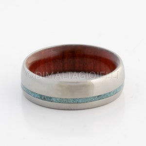 May include: A silver titanium ring with a red wood inlay and a turquoise stone inlay.
