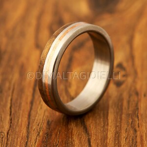 May include: A silver ring with a wooden inlay and two thin gold bands. The ring is on a wooden surface.