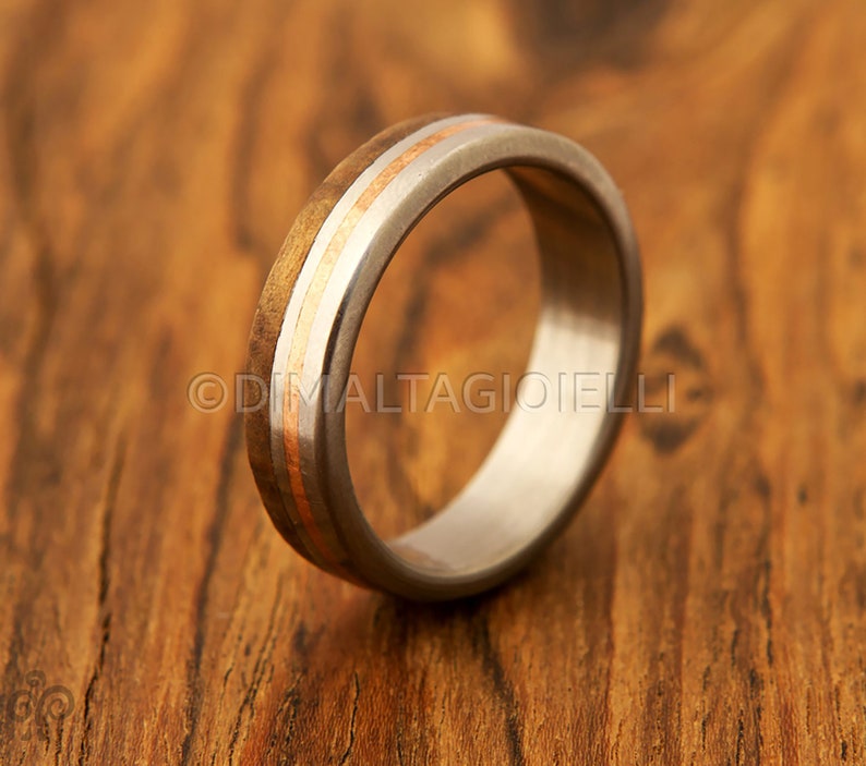 May include: A silver ring with a wooden inlay and two thin gold bands. The ring is on a wooden surface.