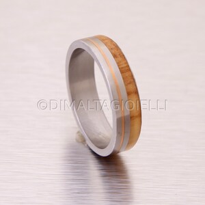 May include: A silver ring with a thin band of wood and two thin gold bands.