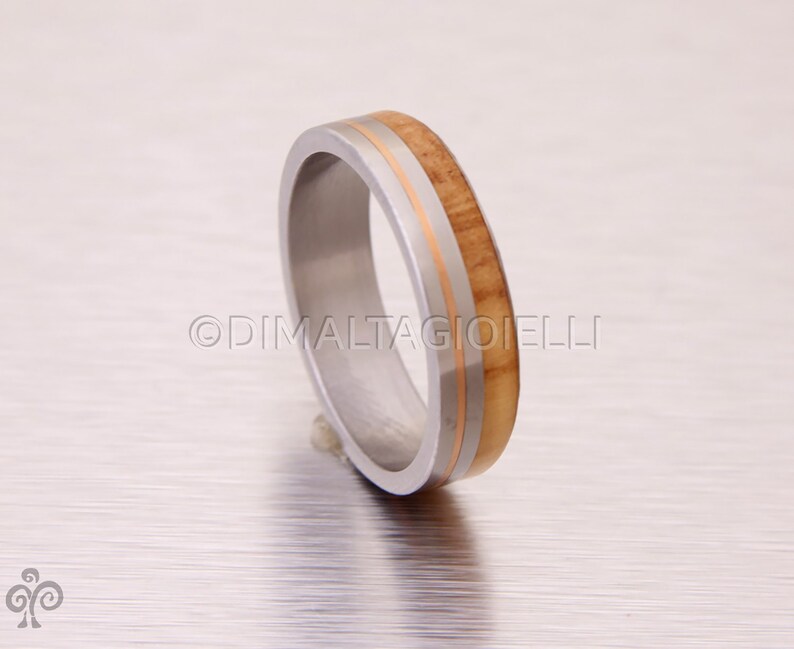 May include: A silver ring with a thin band of wood and two thin gold bands.