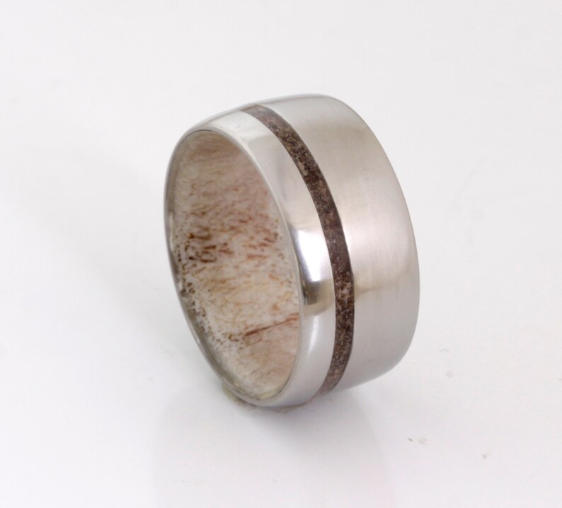 May include: A silver ring with a brown wood inlay. The ring is wide and has a rounded profile.