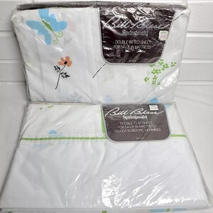 May include: Two packaged Bill Blass Springmaid double bed sheet sets. One is a fitted sheet for a 54x76 inch mattress, the other is a flat sheet. The sheets are white with floral and butterfly patterns in blue, orange, and green.