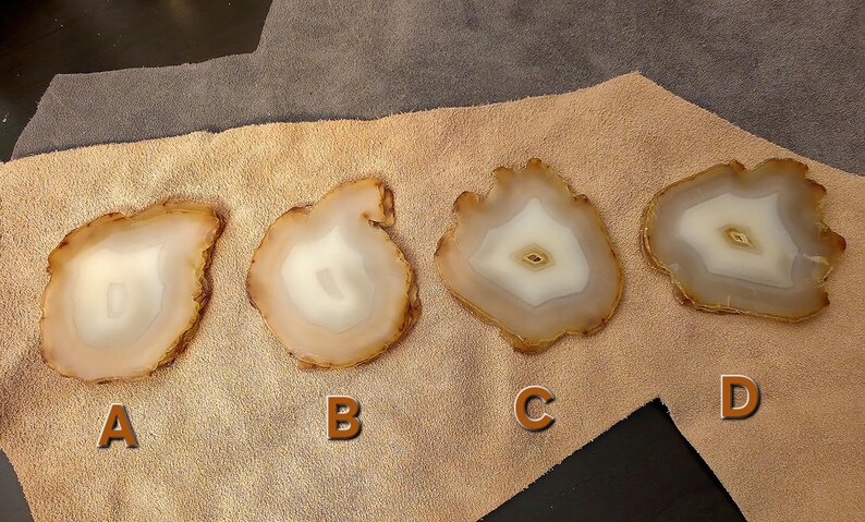 May include: Four agate coasters with a natural, organic shape. Each coaster features a white centre surrounded by bands of tan and brown. The coasters are labelled A, B, C, and D.