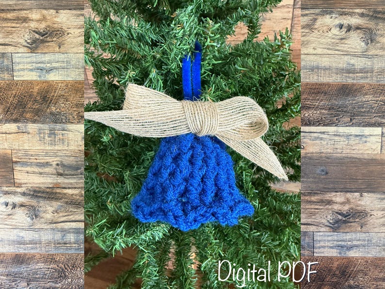 May include: A blue crocheted bell Christmas tree ornament with a burlap bow. The ornament is suspended by a blue ribbon. The text "Digital PDF" is visible at the bottom, against a backdrop of fir.