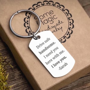 Puede incluir: Un llavero con una placa plateada. La placa tiene grabada la frase "Drive safe handsome. I need you here with me. I love you. -Sarah". El llavero descansa sobre una caja marrón.